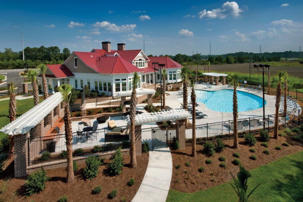 Clubhouse with red roof, pool, and palm trees in an outdoor setting at Grand Oaks at Ogeechee River in Savannah, GA.