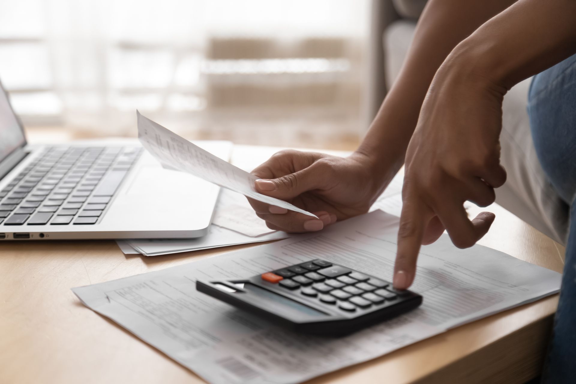 Person using a calculator with a bill and laptop on a table.