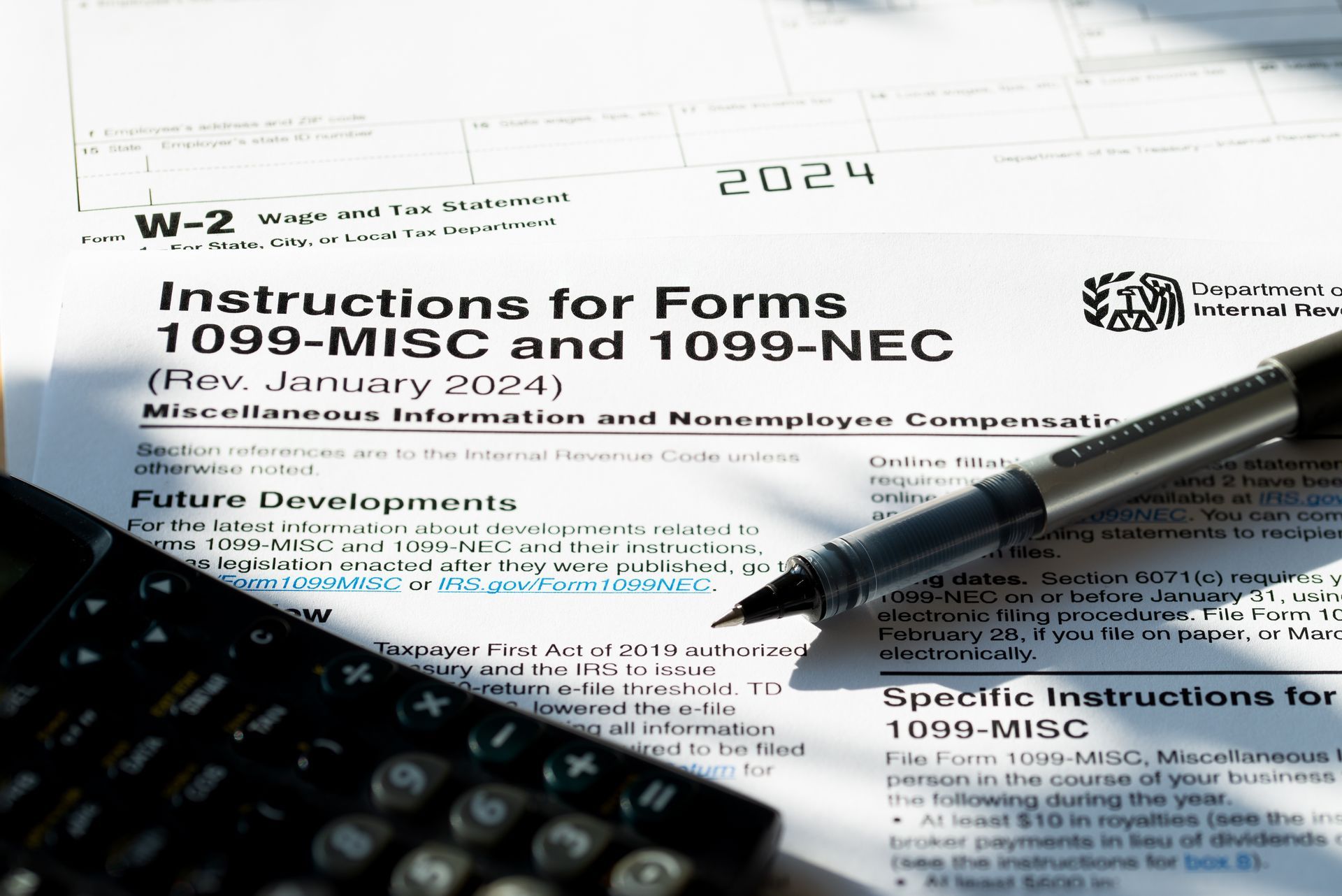 Tax forms 1099-MISC and 1099-NEC instructions with a pen and calculator.