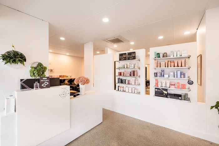White hair salon interior with product displays and reception desk.