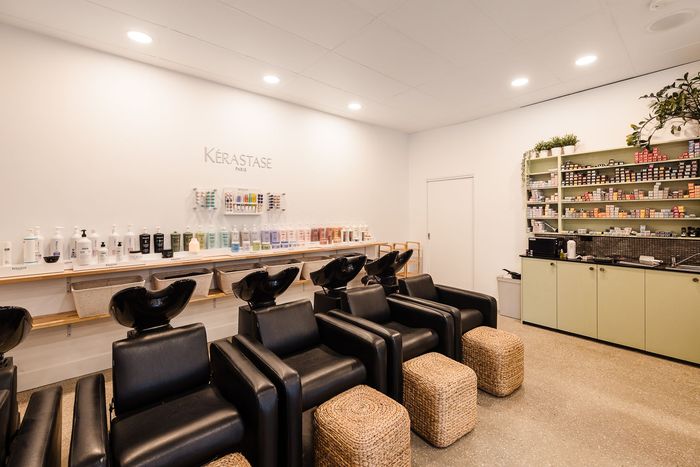 Hair salon interior with wash stations, black chairs, and product display. Bright, white walls and flooring.