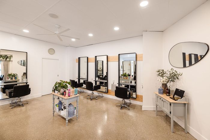Hair salon interior with mirrors, chairs, and styling stations. White walls, terrazzo floors.