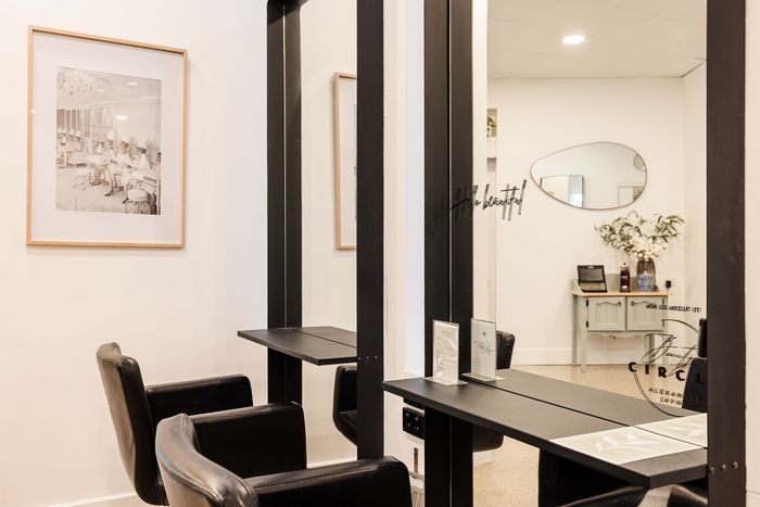 Hair salon interior with mirrors, black chairs, and artwork.