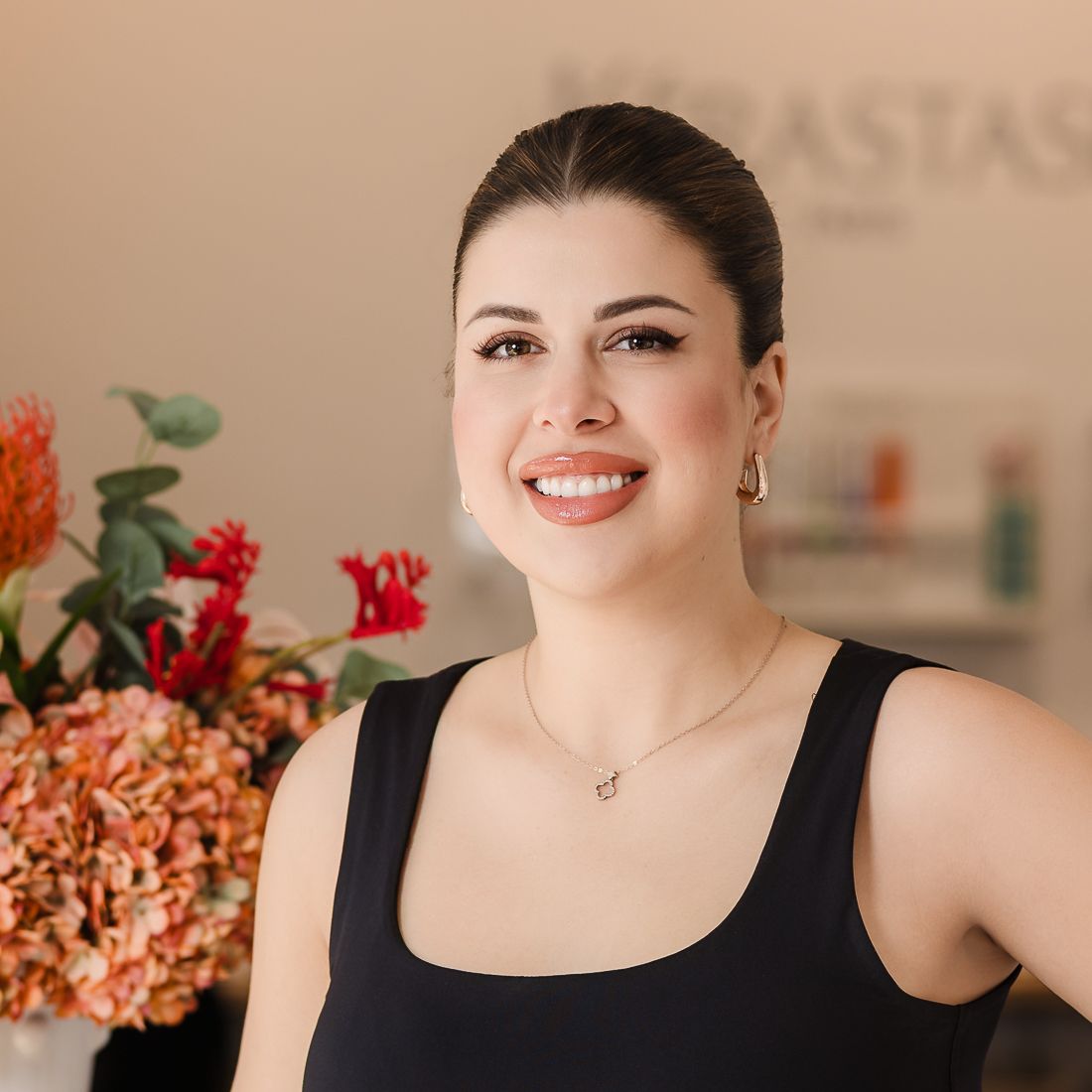 Woman with long dark hair, wearing a black shirt, smiles in a salon.