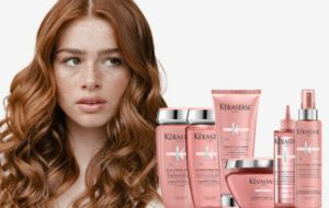 Woman with red wavy hair and freckles, posing with pink Kerastase hair products.