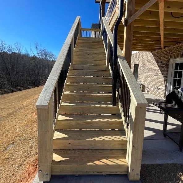 Wooden outdoor staircase leading up to a deck, with dark metal railings. Sunny, clear sky.