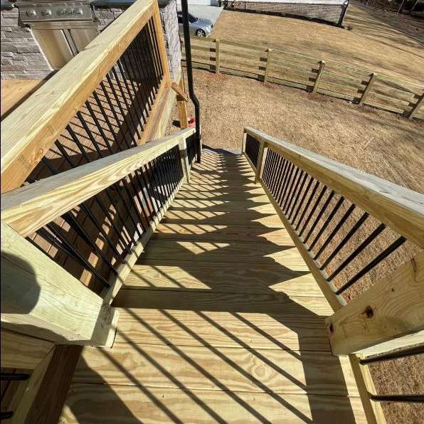 Wooden outdoor staircase with black metal railings, leading down to a yard with a fence.