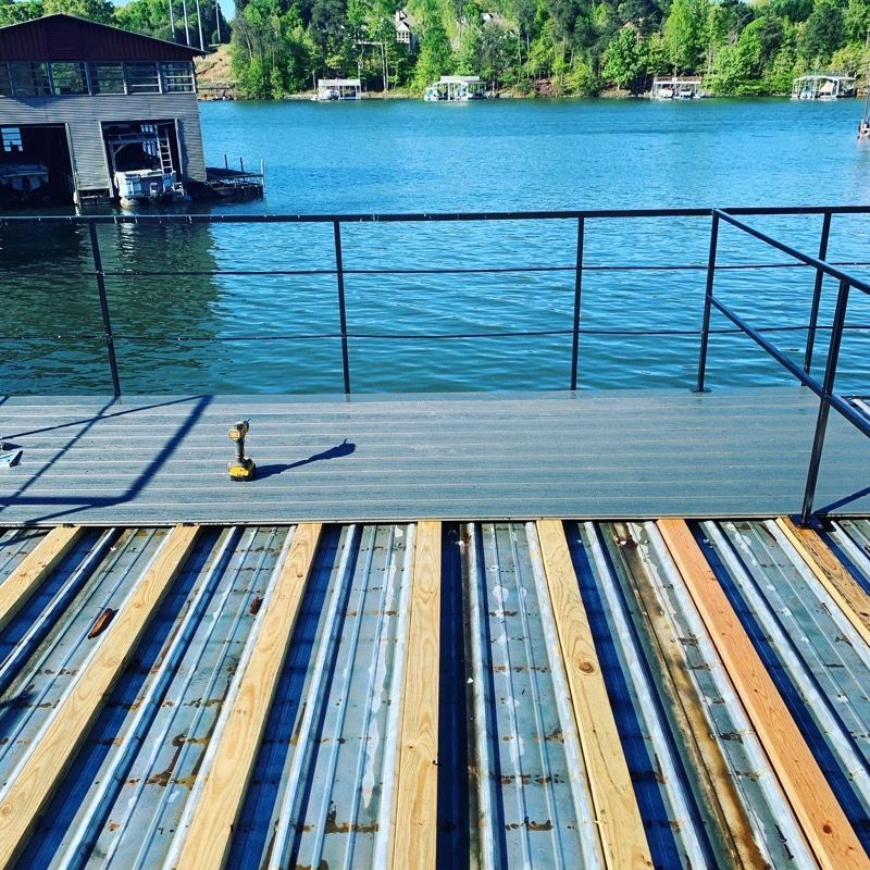 Deck construction over water with partially installed gray composite planks, railing, and boat in the background.