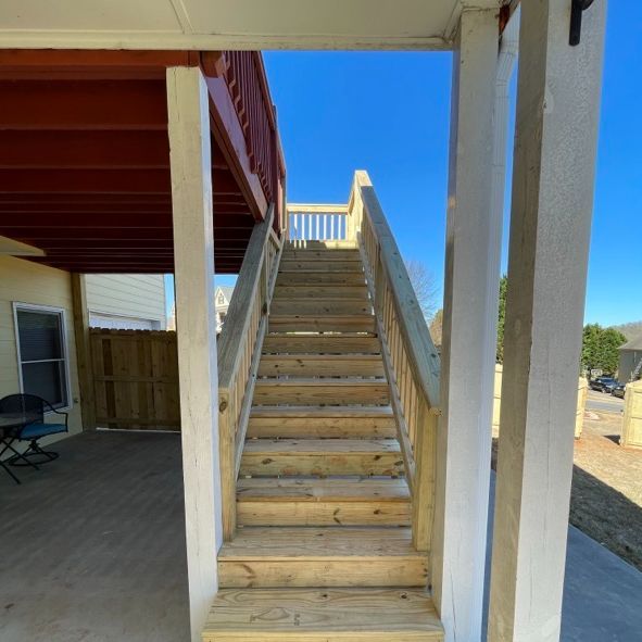 Wooden outdoor staircase leading up to a deck, viewed from underneath. Sunny day.