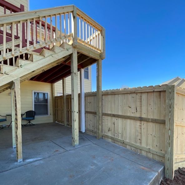 Wooden deck with stairs, supported by posts, over a concrete patio next to a wooden fence.
