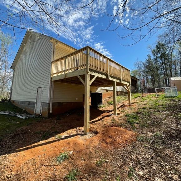 Elevated wooden deck attached to a house with exposed support posts on a sunny day.