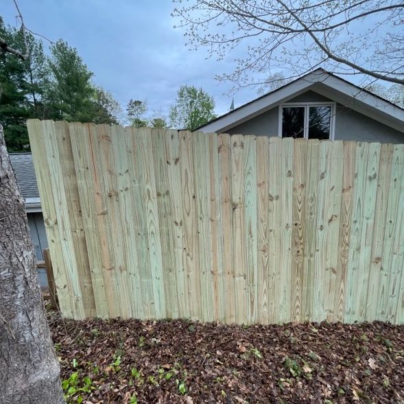 Wooden fence in backyard, with leaflitter on ground, house in background.