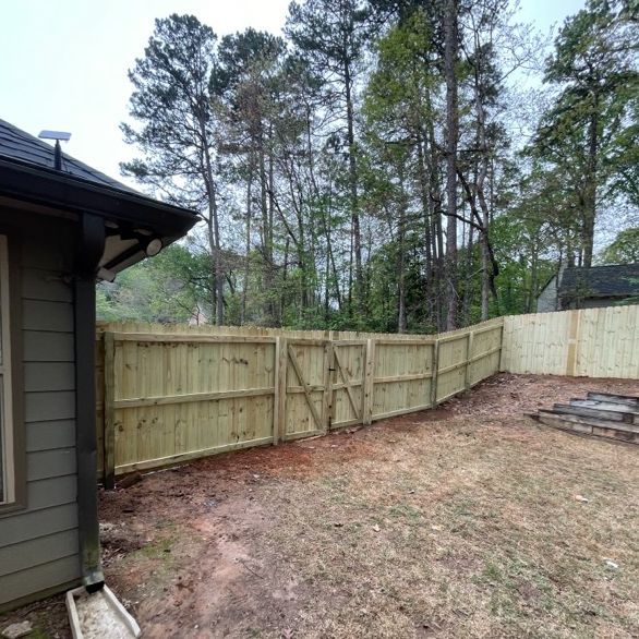 Wooden fence in a backyard with a gate, next to a house and trees.