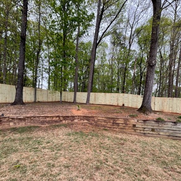 Backyard with wooden fence, trees, and terraced retaining wall.