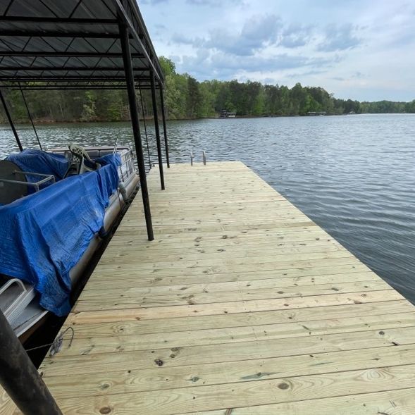 Dock extending into a lake, with a covered boat, and trees in the background under a cloudy sky.