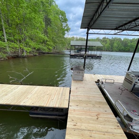 Wooden docks extend into a lake, a pontoon boat is docked. Trees line the shore.