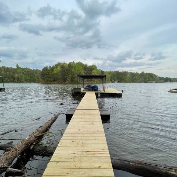 Wooden dock extending into a lake with a covered boat slip. Overcast sky and trees in the background.