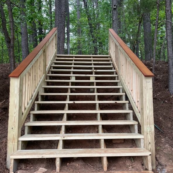 Wooden staircase in a forest setting with a light wood build and a dark wood top rail.