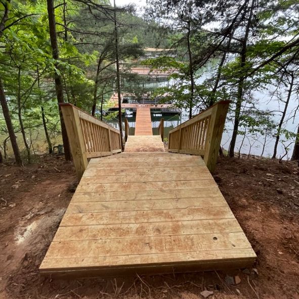 Wooden stairs lead to a dock on a lake surrounded by trees.