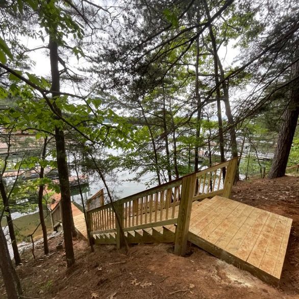 Wooden staircase descending a wooded hillside towards a lake; railings and landing present.