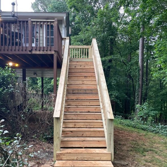 Wooden staircase leading up to a deck attached to a house, surrounded by trees.