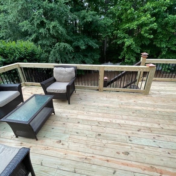 Outdoor wooden deck with patio furniture; lush green trees in the background.