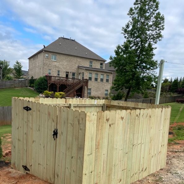 Wooden fence enclosure in a yard with a large brick house in the background.