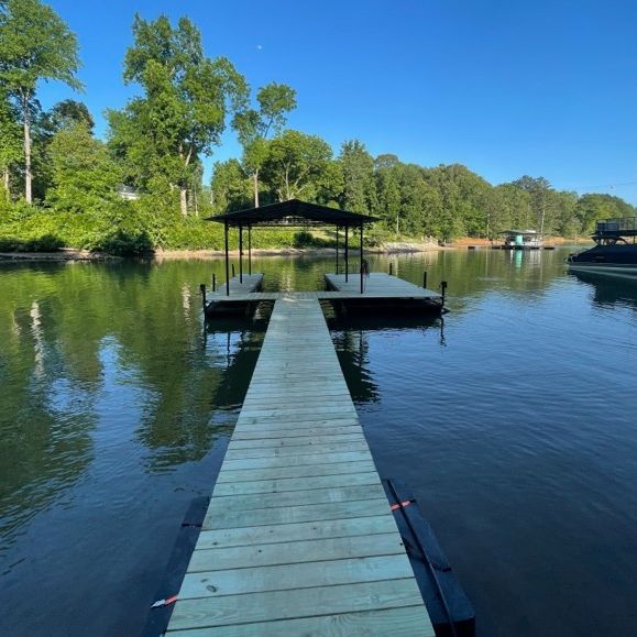 Wooden dock extending into calm water, with a covered boat slip and trees on the shore.