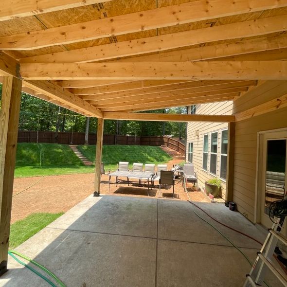 Patio with a wooden pergola; tables, chairs, and house in the background.