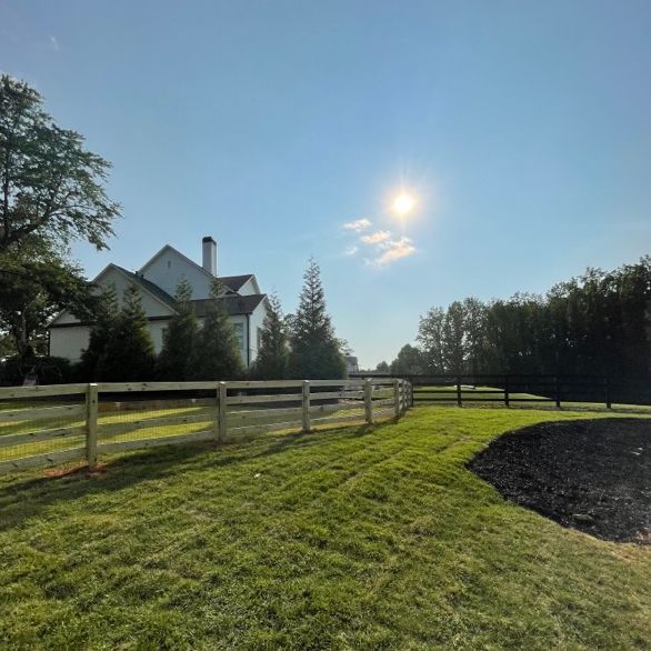 A sunny day with a white house, wooden fence, and green grass.