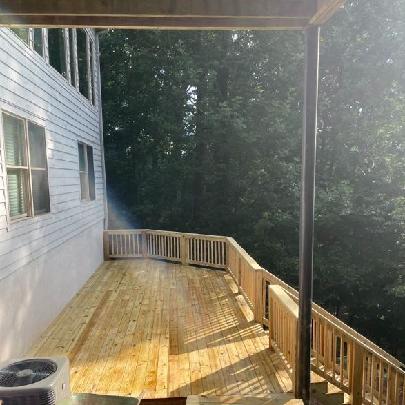 Wooden deck attached to a white house, surrounded by railings and trees.