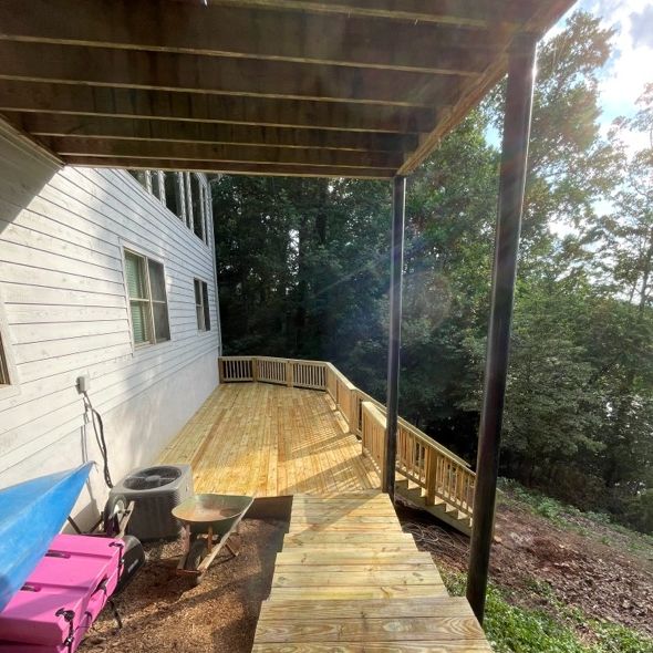 Wooden deck attached to a white house with steps leading down to a wooded area.