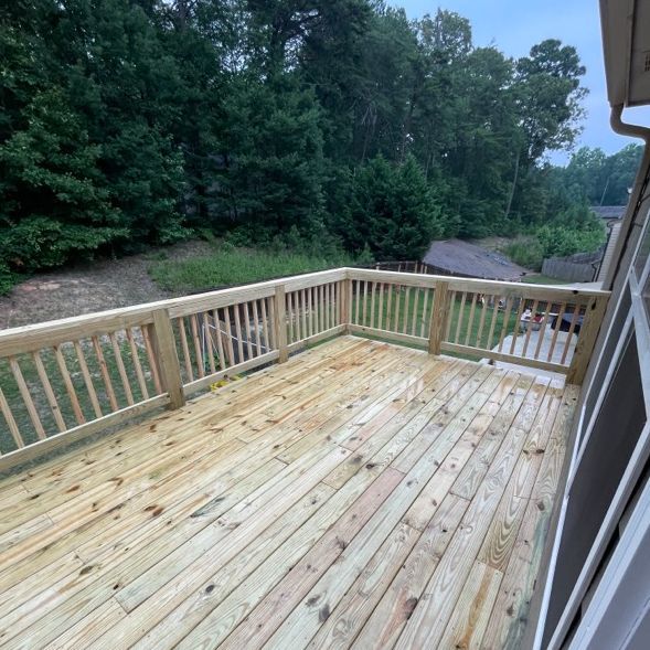 Newly built wooden deck overlooking a wooded area. The deck has railings and is slightly wet.
