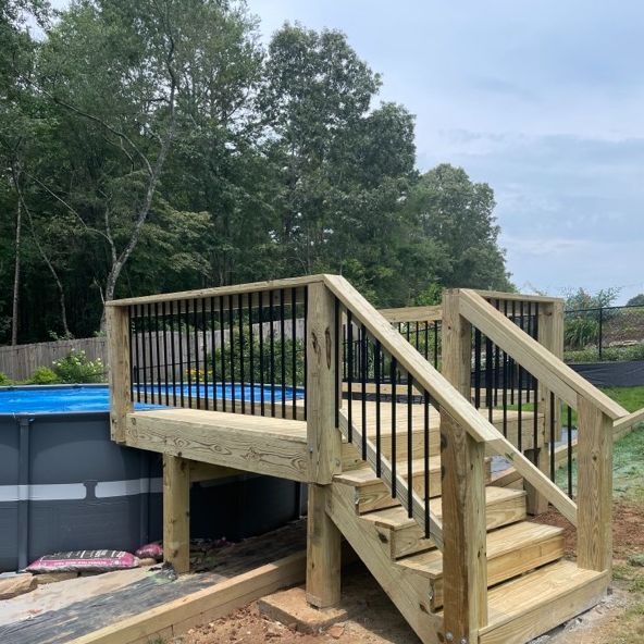 Wooden deck with steps next to an above-ground pool; black railing posts.