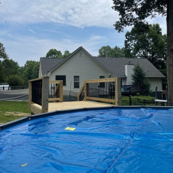 Backyard scene: Above-ground pool in front of deck attached to a light-colored house.