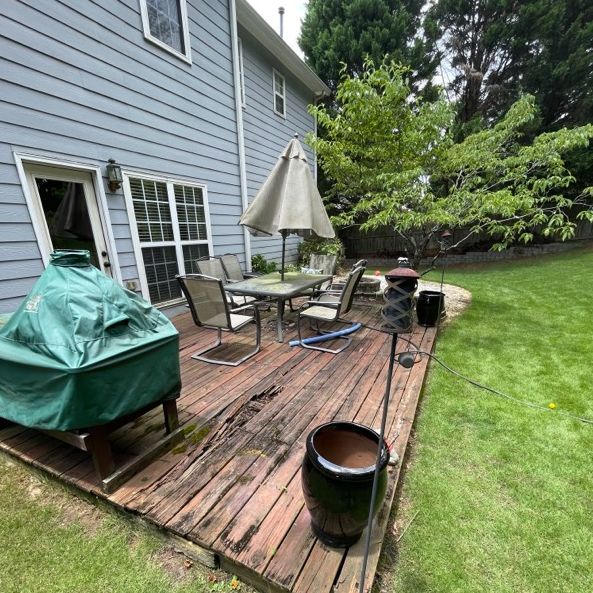 Wooden deck with patio furniture, grill, and Big Green Egg, beside a light blue house and green lawn.
