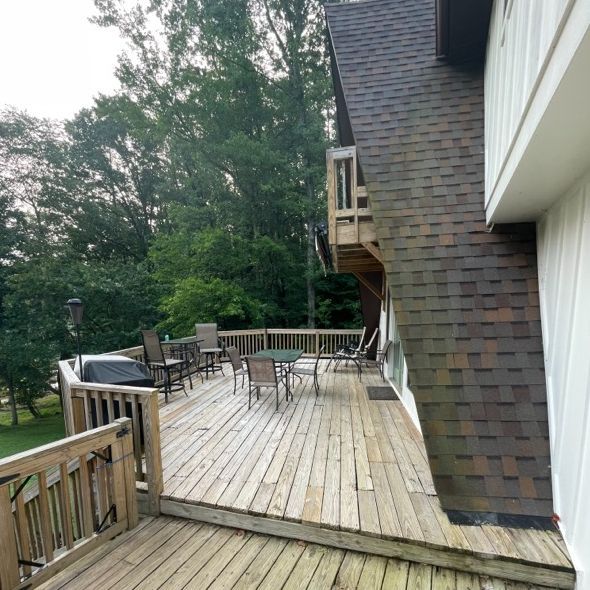 Wooden deck with outdoor furniture, beside a chimney and trees in the background.