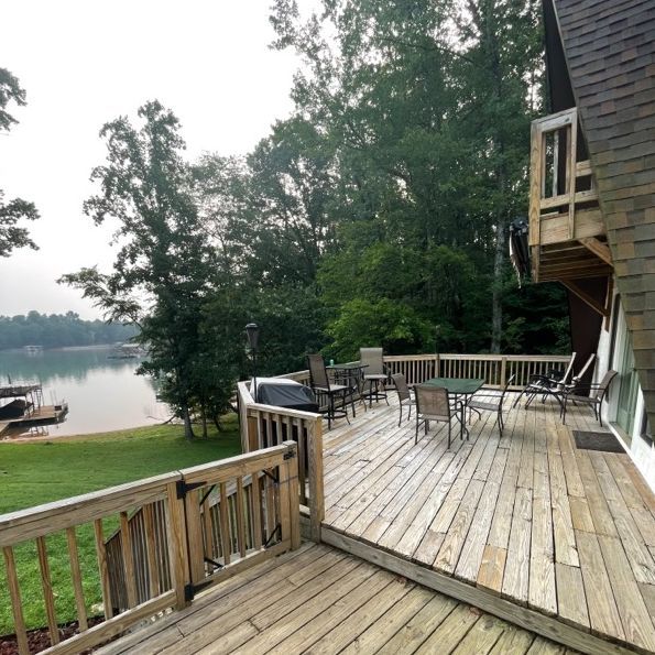 Wooden deck with outdoor furniture overlooking a lake and trees.