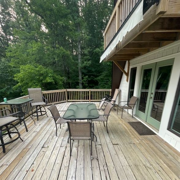 Wooden deck with patio furniture, overlooking a wooded area. The house has green doors and a balcony.