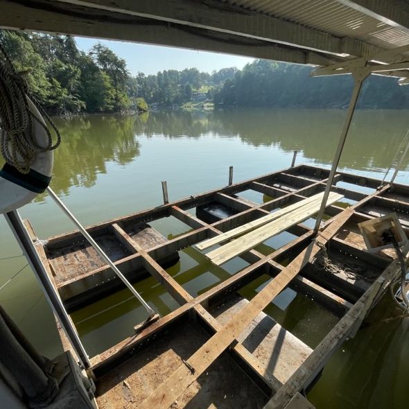 Dilapidated dock with exposed frame submerged in murky water; trees in the background.