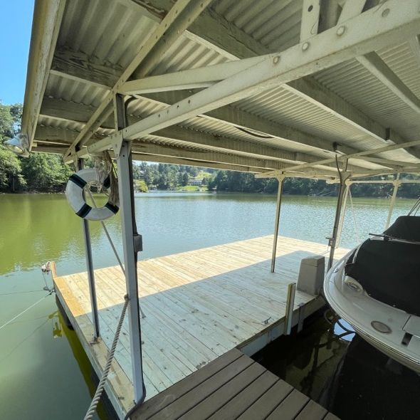 A wooden dock with a covered roof extending into a lake, boat docked on the side.
