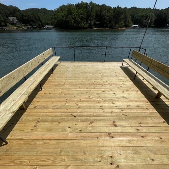 Wooden dock with benches overlooking a lake, blue sky, trees in the background.