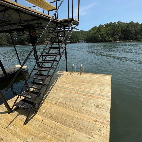 Dock with metal stairs leading to a platform with water access. Wood decking, metal frame. Sunny day.