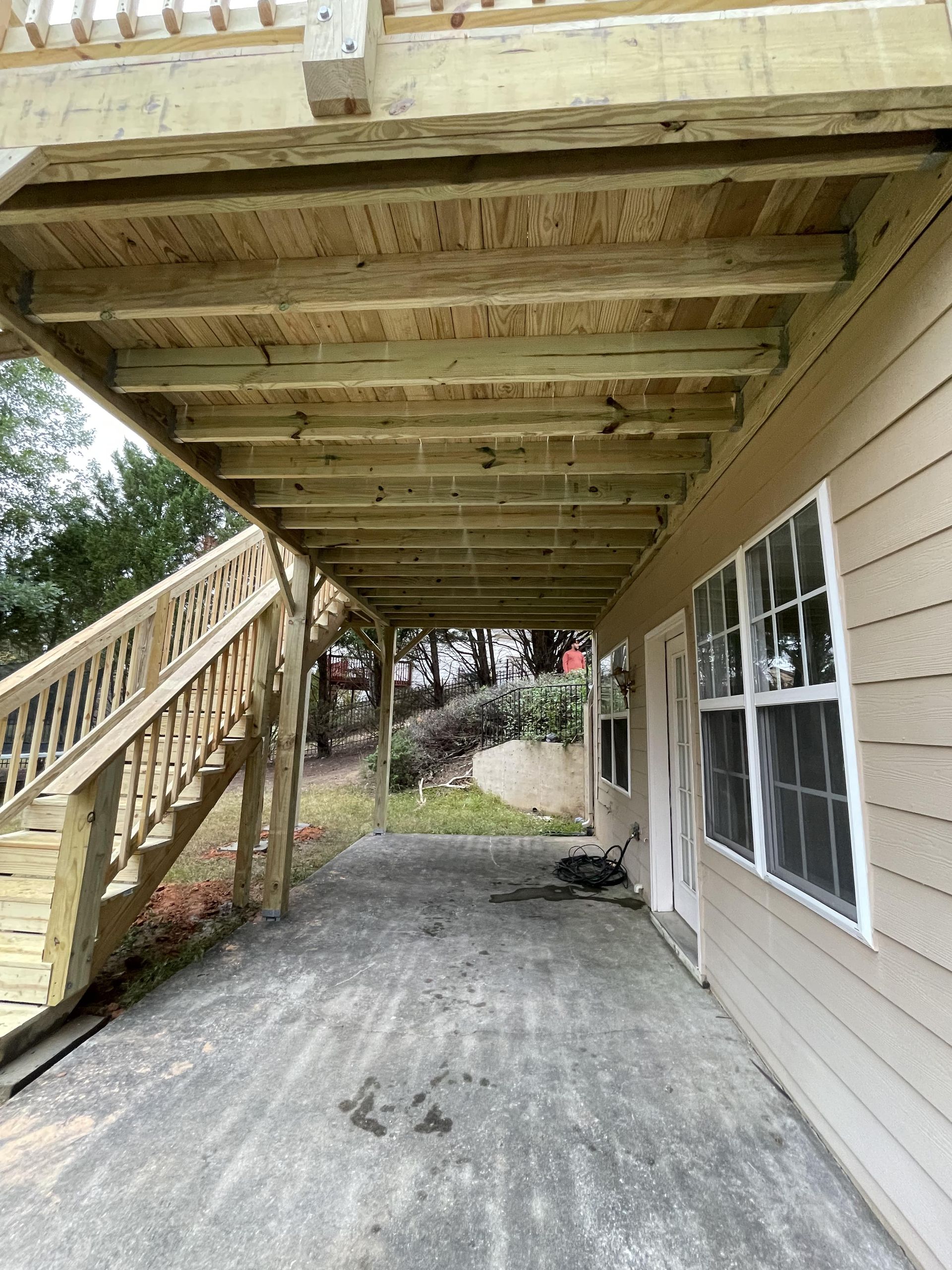Exterior view beneath a wooden deck with stairs. A concrete patio is below with a tan-sided building.