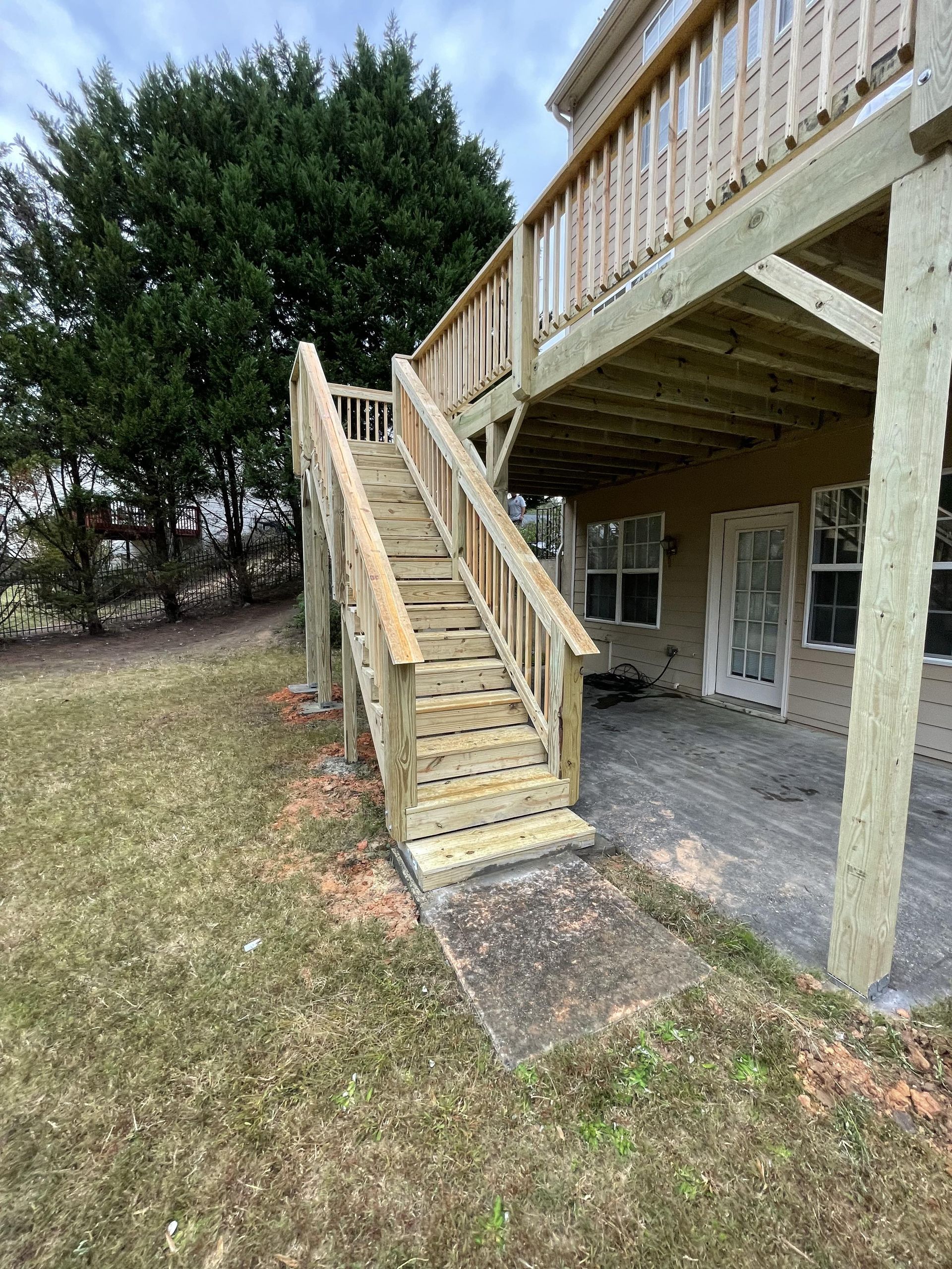 Wooden deck stairs leading to a raised deck, next to a house on a grassy lawn.