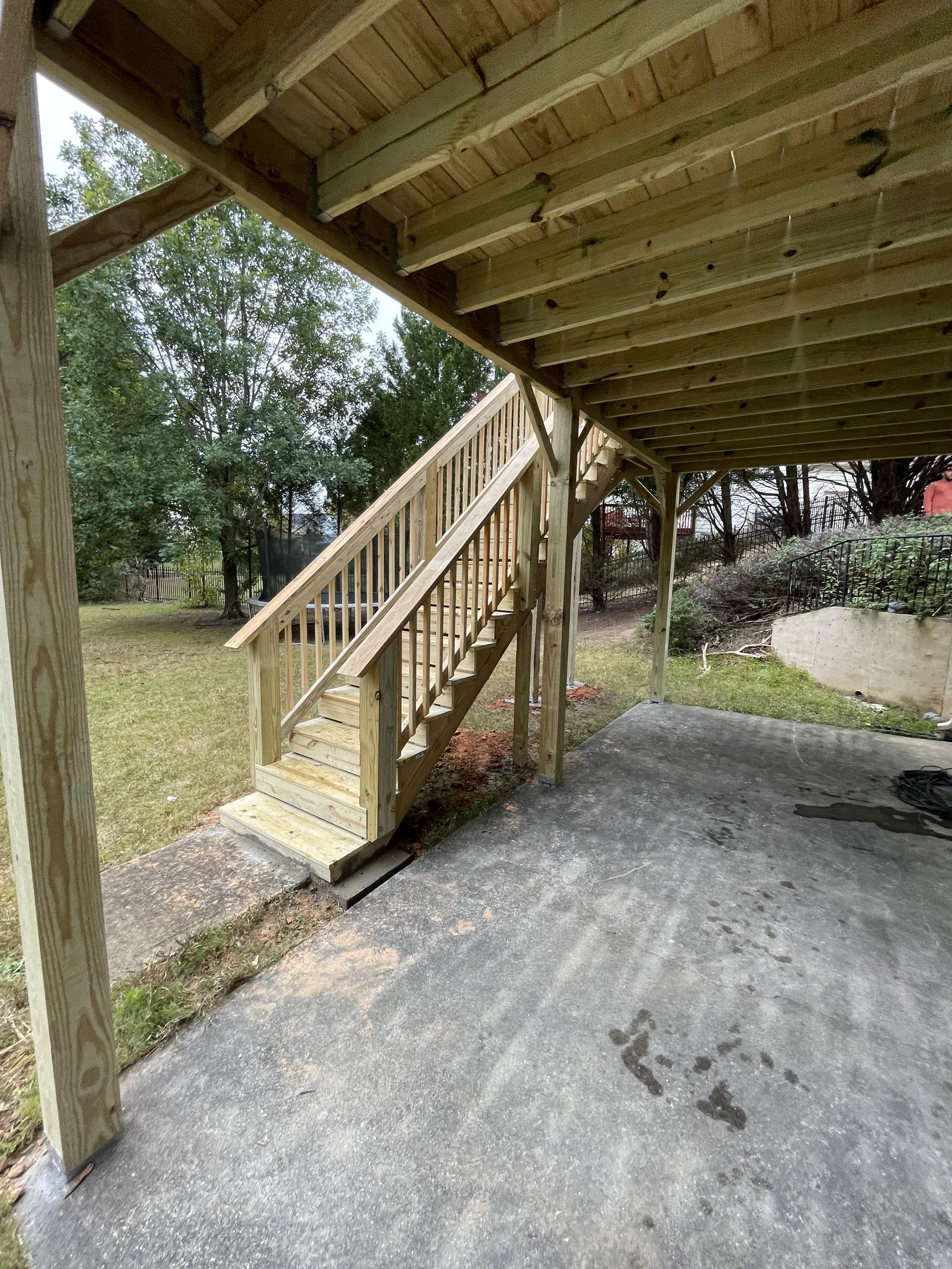 Wooden staircase leading up to a covered deck, situated over a concrete slab.