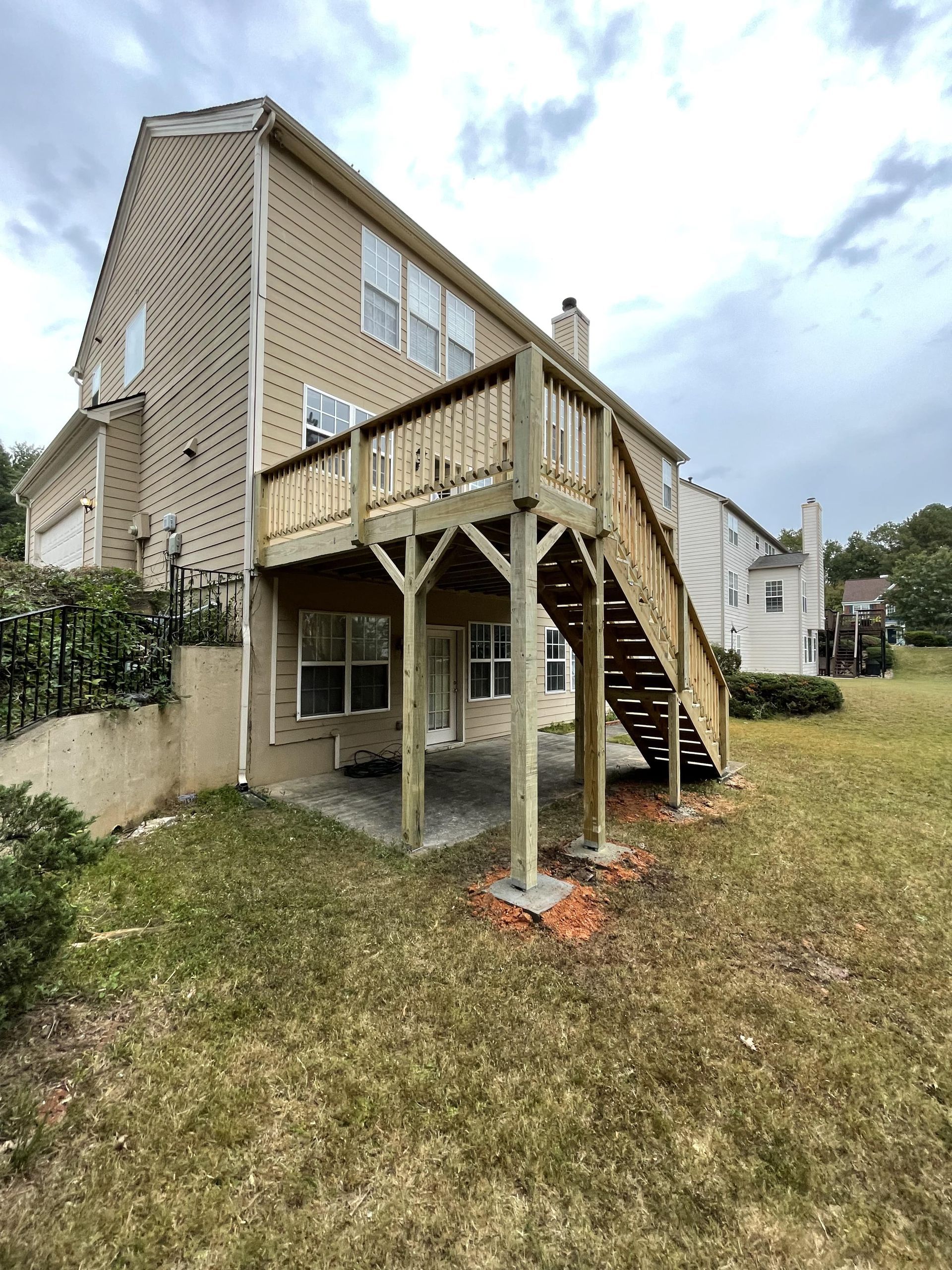 Two-story house with a wooden deck and stairs leading to a grassy backyard.