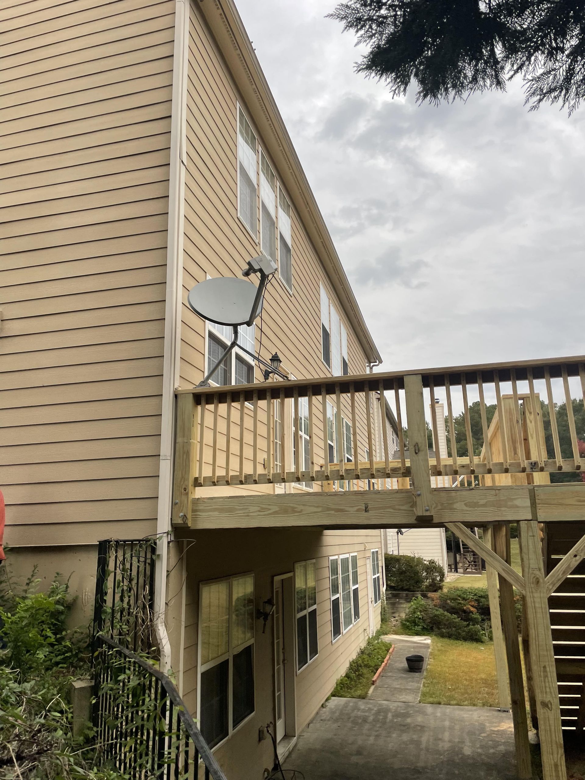Side view of a two-story building with a wooden deck. A satellite dish is mounted on the siding.