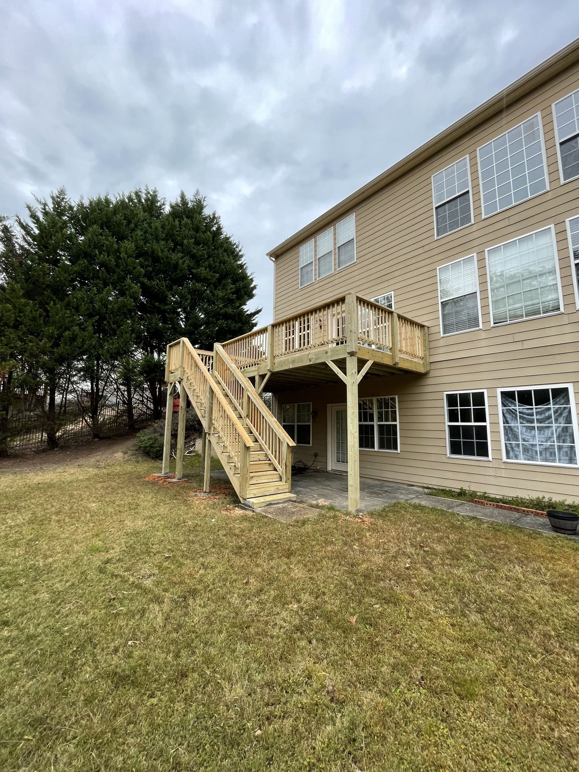 Wooden deck with stairs attached to a two-story beige house under a cloudy sky.