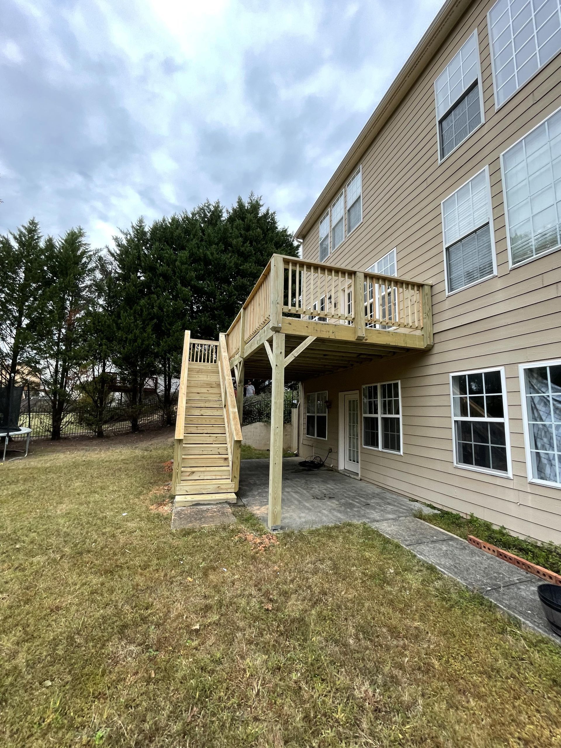 Wooden deck with stairs attached to a beige multi-story building. Overcast sky, grassy yard.